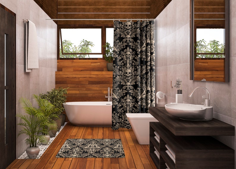 Op de afbeelding: Een badkamer met een wit bad, een wit toilet en een donkerhouten wastafel met een witte wastafel. Het douchegordijn is zwart met een wit schedel- en kruisbeenderenpatroon. De vloer is van hout.