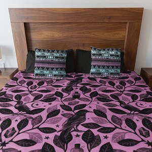 May include: A pink and black bedding set with a pattern of leaves, ravens, stars, and crystals. The bedding set includes two pillowcases with a geometric pattern.