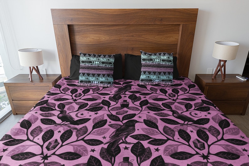 May include: A pink and black bedding set with a pattern of leaves, ravens, stars, and crystals. The bedding set includes two pillowcases with a geometric pattern.