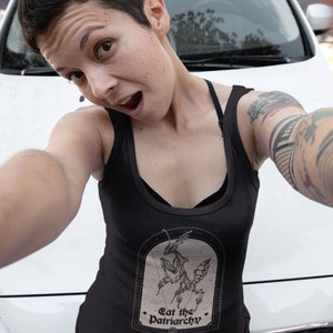 Może przedstawiać: Czarny top na ramiączkach z grafiką modliszki i tekstem "Eat the Patriarchy".
