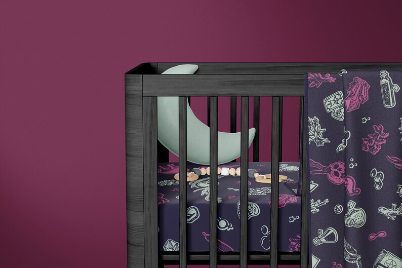 May include: A black cot with a white and blue patterned sheet and a matching blanket. The blanket features a design of potion bottles, herbs, and other magical items. A crescent moon shaped pillow is in the cot.