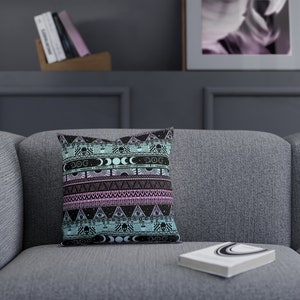 May include: A decorative throw pillow with a black and white geometric pattern featuring skulls, moons, and eyes. The pattern is on a light blue and pink background.