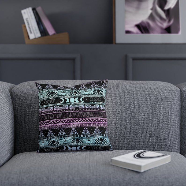 May include: A decorative throw pillow with a black and white geometric pattern featuring skulls, moons, and eyes. The pattern is on a light blue and pink background.