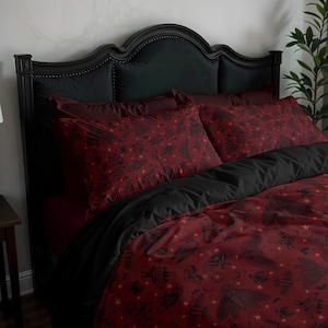 Op de afbeelding: Een beddengoedset bestaande uit een dieprode dekbedovertrek en bijpassende kussenslopen met een herhalend zwart patroon van diverse mottensoorten, kleine sterren en maansikkels, gecombineerd met een effen zwart laken en een zwart hoofdbord.
