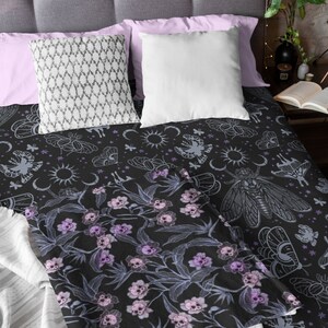 Folded goth blanket on bed with decorative pillows and showing the pink, purple and blue flower skulls.