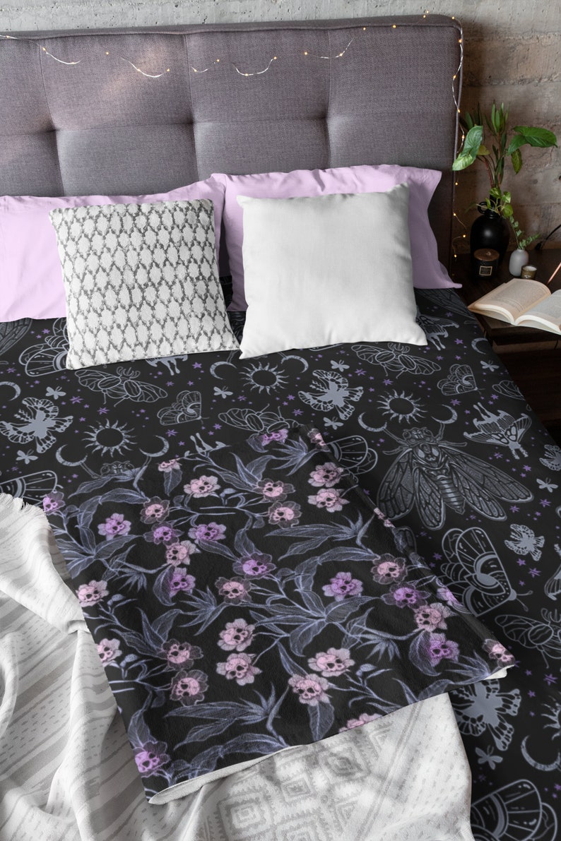 Folded goth blanket on bed with decorative pillows and showing the pink, purple and blue flower skulls.