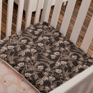 May include: A white crib with a black and white skull and floral patterned fitted sheet and a pink fitted sheet with white swans.