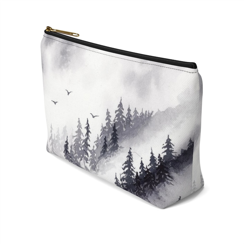 May include: A white canvas makeup bag with a black zipper and a watercolor print of a misty forest scene with black trees and birds flying in the sky.