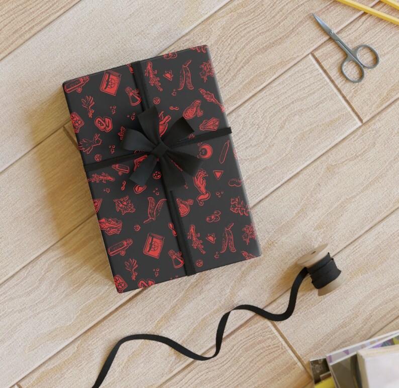 May include: Black gift wrap with a red and white pattern of various symbols and designs. A black ribbon is tied around the gift wrap with a bow.