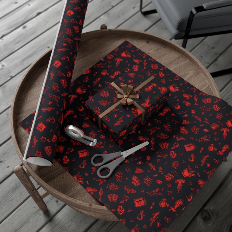 May include: Black and red wrapping paper with a repeating pattern of various symbols, including a hand holding a knife, a skull, a potion bottle, and a crescent moon. A brown gift box with a red ribbon is on top of the wrapping paper.