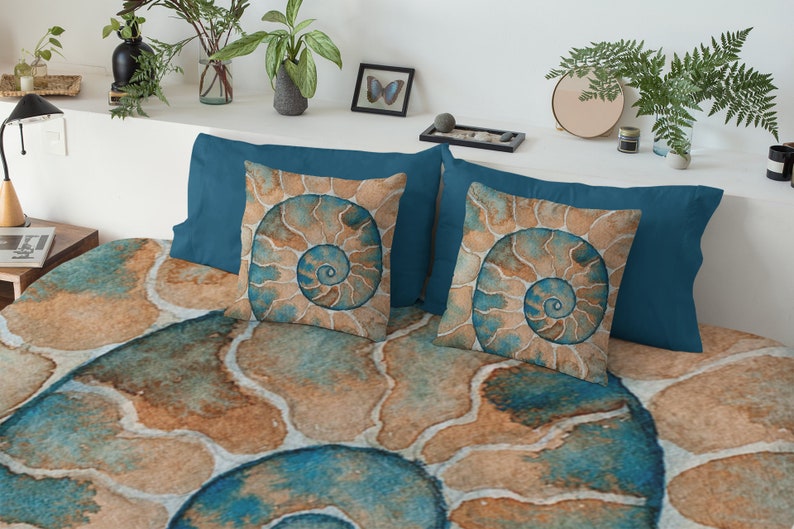 May include: A teal blue bedding set with a large, abstract, watercolor-style print of a nautilus shell. The bedding set includes two pillowcases with a smaller print of the nautilus shell.