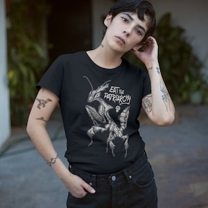 Może przedstawiać: Czarny T-shirt z grafiką modliszki i tekstem "Eat the Patriarchy".