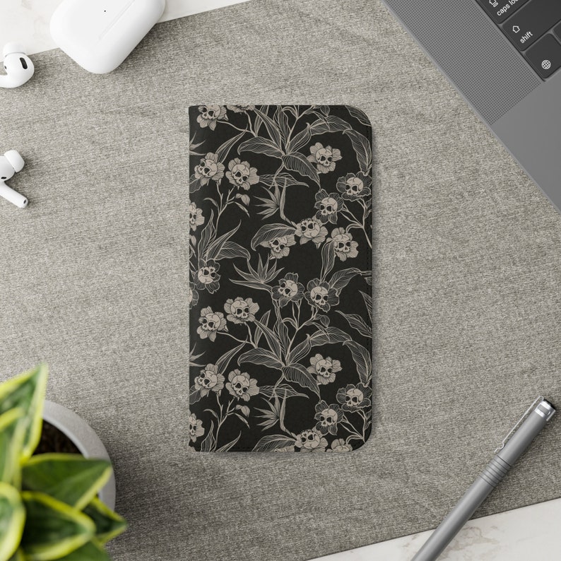 May include: A black phone case with a white floral pattern featuring skulls. The flowers are stylised and have a vintage look.