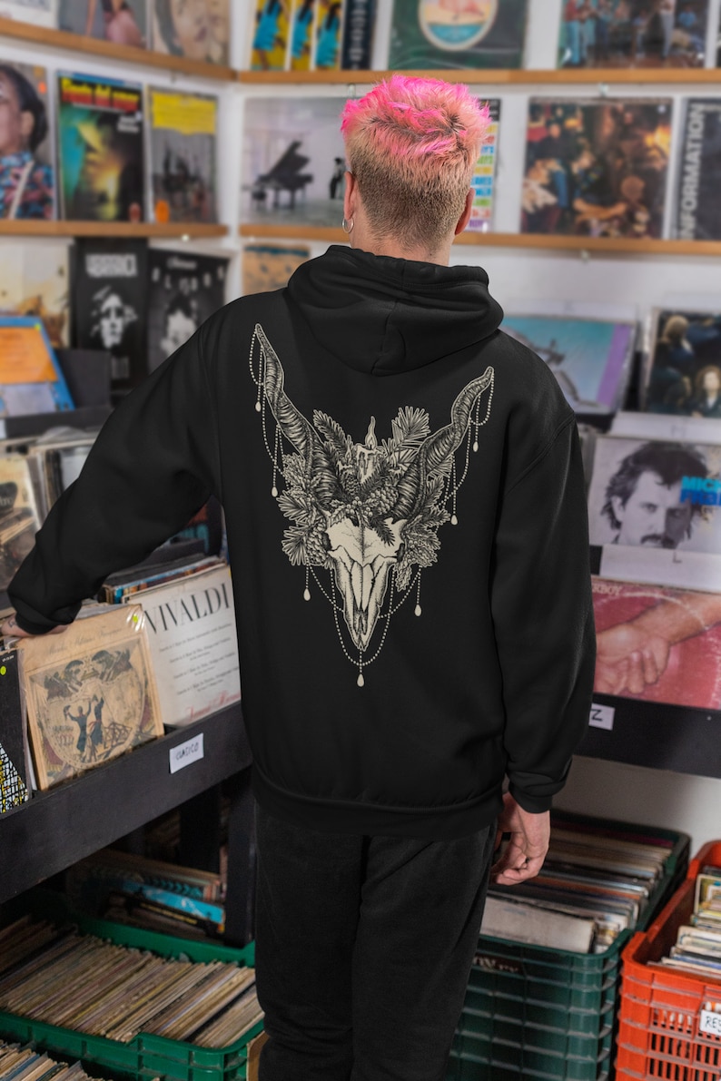 May include: Black hoodie featuring a detailed graphic of a skull with horns, floral elements, and beaded accents on the back. The design is in shades of cream and beige. The hoodie is a casual garment.