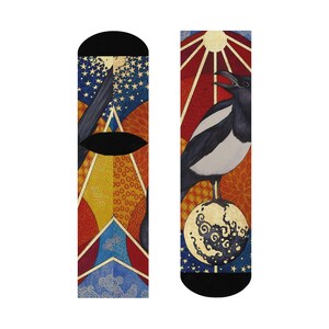 May include: A pair of socks with a colorful, abstract design. One sock features a magpie standing on a sphere with a sun and stars in the background. The other sock features a similar design with a different color scheme.