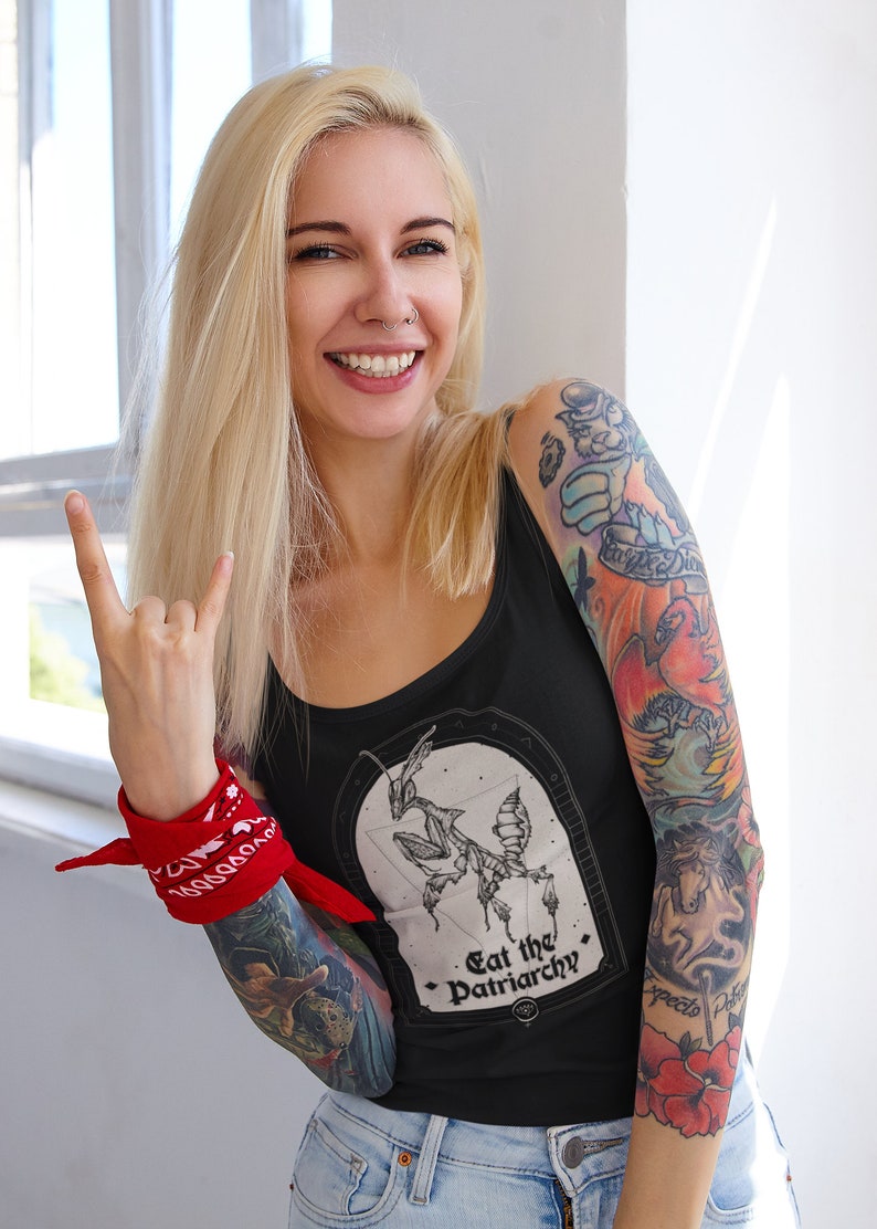 Może przedstawiać: Czarny top na ramiączkach z grafiką modliszki i tekstem "Eat the Patriarchy". Modelka nosi top i ma czerwoną chustkę na nadgarstku.