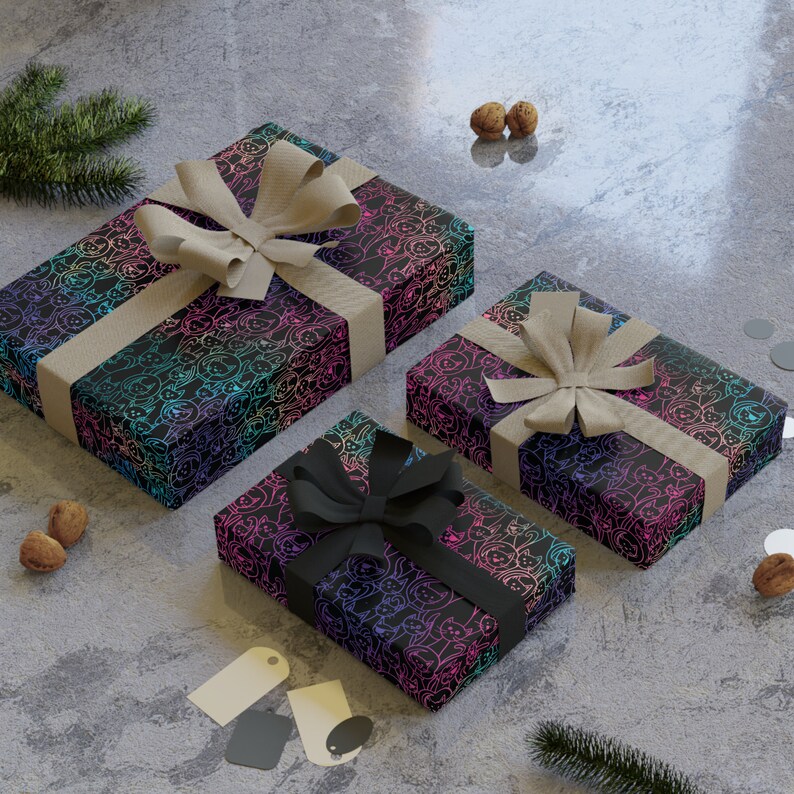 K&ouml;nnte beinhalten: Drei Geschenkboxen, die in schwarzes Papier mit einem Regenbogenmuster aus Katzen eingewickelt sind. Die Boxen sind mit braunem und schwarzem Band gebunden.