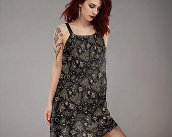 May include: Black slip dress with a beige moth and celestial pattern. The dress has a scoop neckline, thin black straps, and a knee-length hemline. The fabric drapes loosely. The dress is worn with black fishnet stockings.