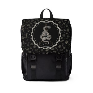 Puede incluir: Mochila negra con una serpiente blanca y un diseño circular en la parte delantera. El diseño circular tiene una serpiente blanca envuelta alrededor de un triángulo con un símbolo en la parte superior. El fondo de la mochila es negro con un patrón de símbolos blancos.