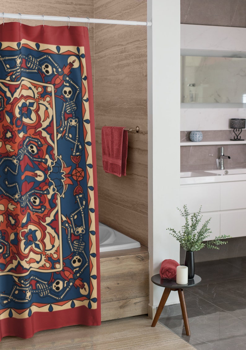 Op de afbeelding: Een rood douchegordijn met een blauw en wit patroon met skeletten die dansen rond een centraal motief. Het gordijn hangt in een badkamer met een wit bad en een houten vloer.