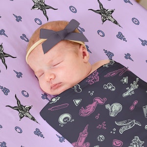 May include: A sleeping baby wrapped in a dark purple swaddle blanket with a black and white pattern of occult symbols. The baby is wearing a purple bow on their head and is lying on a light purple sheet with a similar pattern.