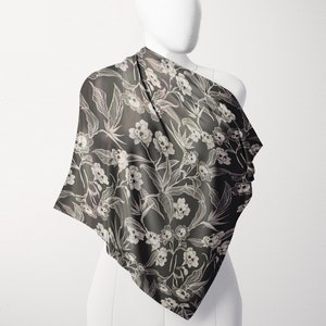 May include: A black and white floral print scarf with a skull design. The scarf is draped over a white mannequin.