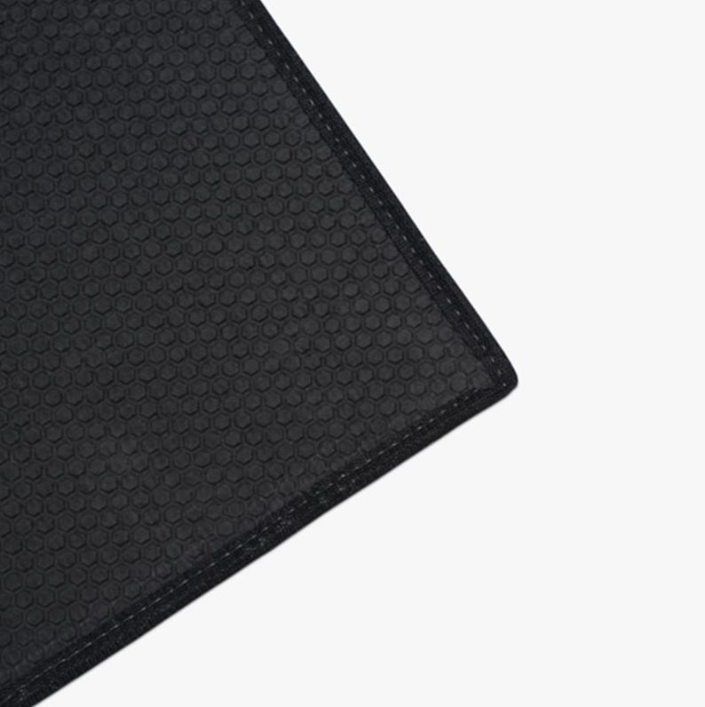 May include: Close-up of a black yoga mat with a textured hexagonal pattern. The mat has a stitched edge.