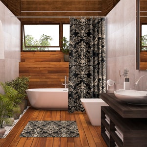 May include: A bathroom with a white bathtub, a white toilet, and a dark wood vanity with a white sink. The shower curtain is black with a white skull and crossbones pattern. The floor is wood and there is a black and white rug with a skull and crossbones pattern.