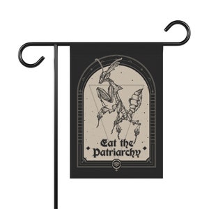 May include: Black and white garden flag with a drawing of a praying mantis in a geometric frame. The text "Eat the Patriarchy" is printed below the mantis.