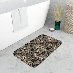 May include: A black and beige bath mat with a skull and crossbones pattern. The pattern is a damask design with skulls and crossbones in the center of each motif.