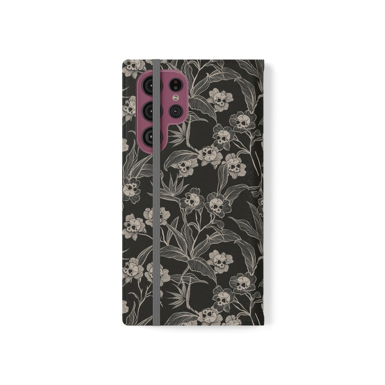 May include: Black phone case with a floral pattern featuring white skulls and leaves.
