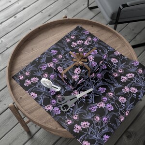 gothic floral gift wrapping paper with pastel skulls on a table with scissors, tape, and a wrapped present with a brown ribbon