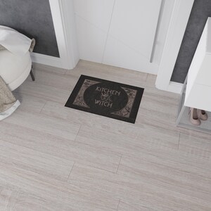 May include: Black doormat with the text "Kitchen Witch" in a white font. The text is surrounded by a circle with a witch's silhouette inside.