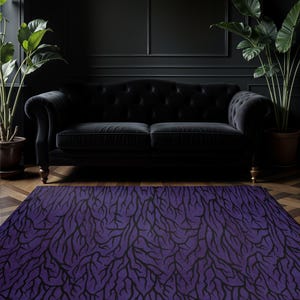 Puede incluir: Una alfombra rectangular morada con un patrón de ramificación negro. La alfombra está colocada frente a un sofá negro con mechones y paredes oscuras. Plantas en macetas a ambos lados del sofá, añadiendo un toque de vegetación.