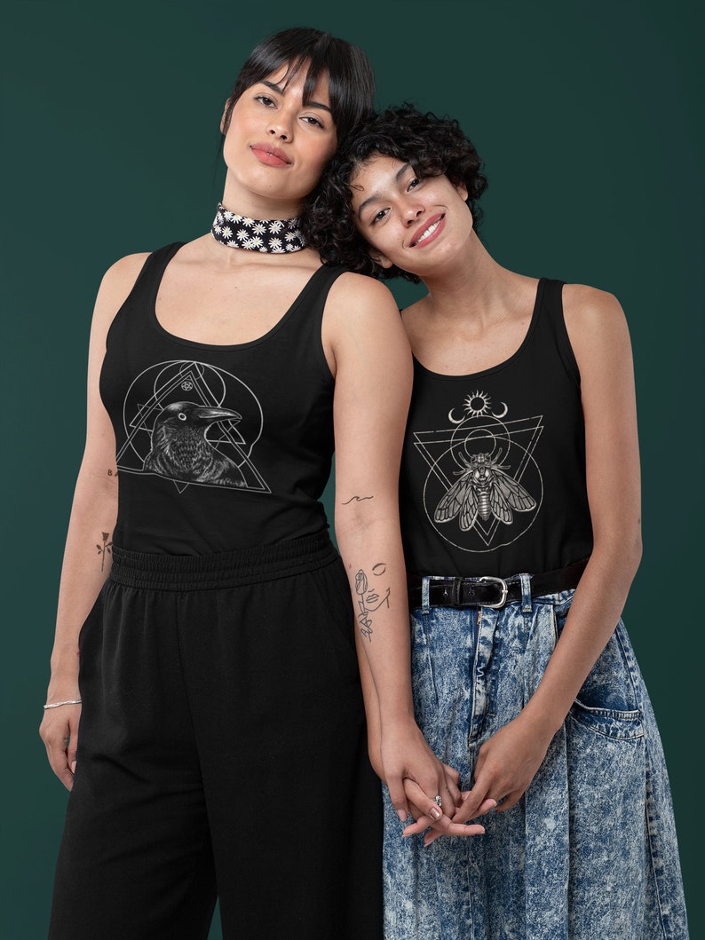 Op de afbeelding: Twee mensen dragen zwarte tanktops met grafische ontwerpen. Het tanktop aan de linkerkant heeft een raaf in een geometrisch ontwerp. Het tanktop aan de rechterkant heeft een mot in een geometrisch ontwerp. Beide mensen houden elkaars handen vast.