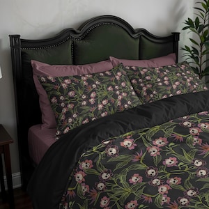 May include: A dark bed set featuring a floral skull pattern. The bedding includes a black duvet cover, pillowcases, and a mauve sheet. The headboard is dark green and the pillows have a dark floral pattern with skulls.