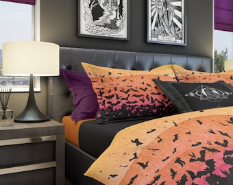 May include: A black bed with a comforter and pillows featuring a pattern of bats on a gradient background of orange, pink, and yellow. The pillows are purple, black, and white with a graphic of a crescent moon and stars.