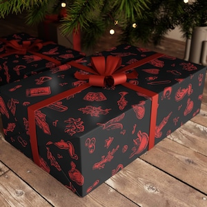 May include: A black gift box with a red ribbon and a red and black patterned design. The pattern includes various symbols and designs, including a compass, a feather, and a skull.