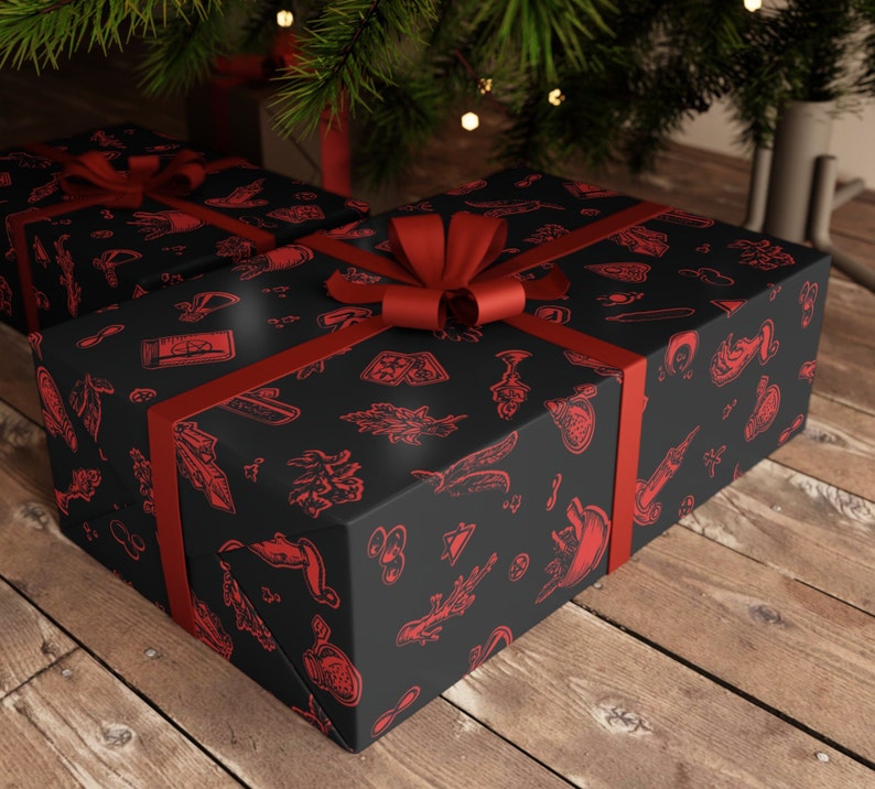 May include: A black gift box with a red ribbon and a red and black patterned design. The pattern includes various symbols and designs, including a compass, a feather, and a skull.