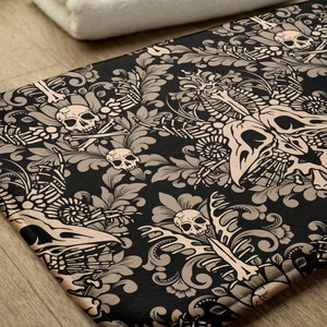 May include: A black bath mat with a beige damask pattern featuring skulls and crossbones, skeletons, and floral designs.