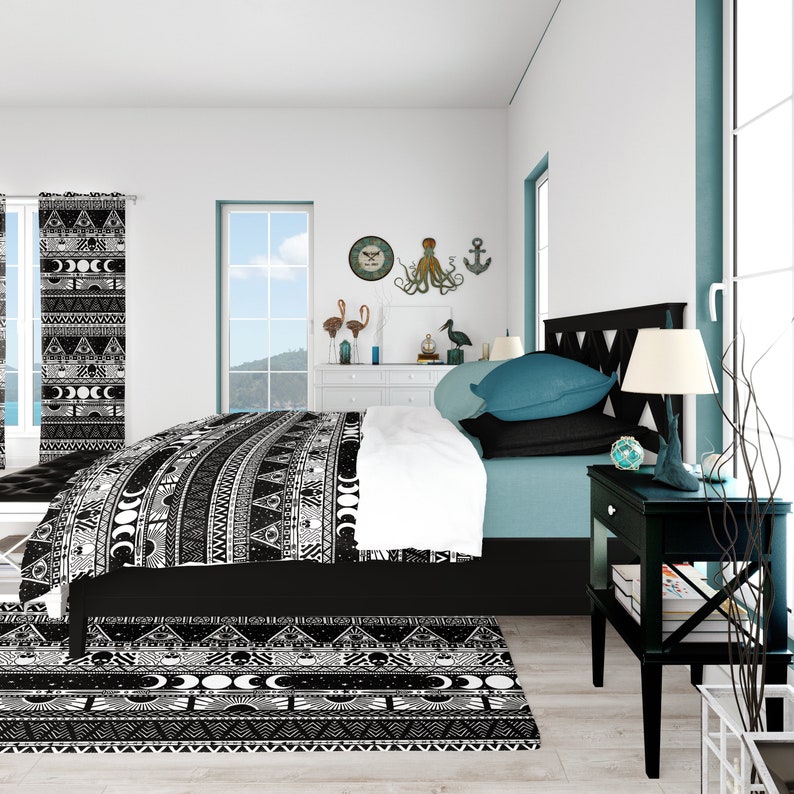 May include: Black and white patterned bedding with a geometric design. The bedding is on a bed with a teal headboard and a black nightstand with a lamp. The room has a white wall with a clock and a nautical decor.