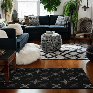 May include: A black and white patterned area rug with a geometric design. The rug is in a living room setting with a black couch, a white fur throw, and a black and white patterned ottoman.