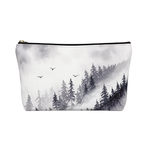May include: A black and white watercolor painting of a misty forest scene with a few birds flying overhead. The painting is printed on a white canvas zippered pouch.