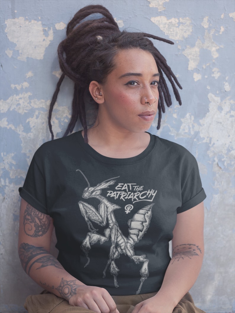 Może przedstawiać: Czarny t-shirt z białym nadrukiem przedstawiającym modliszkę i tekstem "Eat the Patriarchy" z symbolem żeńskim.