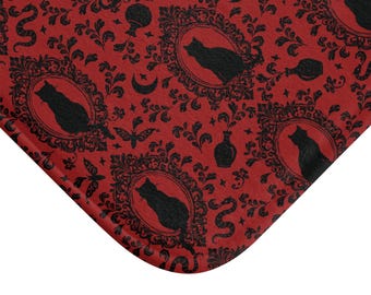 May include: Red bath mat with a black and white damask pattern featuring cats, moons, butterflies, and potion bottles.