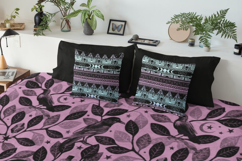 May include: A pink and black patterned bedding set with a design of ravens and leaves. The set includes two throw pillows with a black background and a geometric pattern in shades of blue, pink, and white.