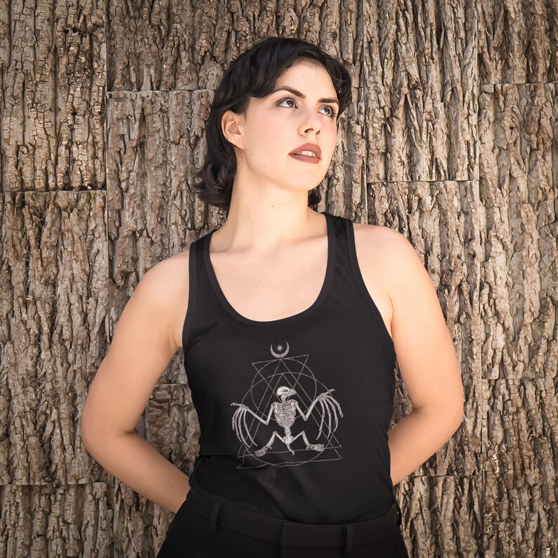 May include: A woman wearing a black tank top with a graphic of a bat skeleton inside a geometric design. The design includes a crescent moon and a triangle.