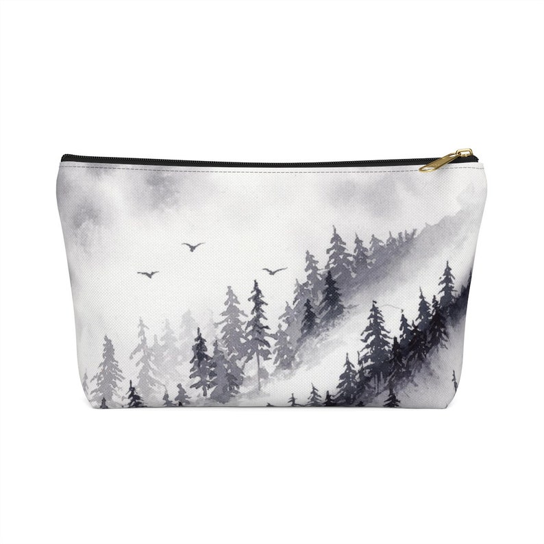 May include: A black and white watercolor print of a misty forest scene with a zippered pouch. The pouch is made of canvas and has a black zipper.