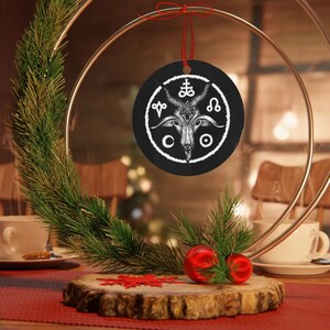 May include: Black and white Christmas ornament featuring a goat head with horns and a pentagram. The goat head is surrounded by a circle with symbols and the letters 'CO'.