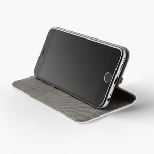 May include: A grey phone case with a black smartphone inside. The case is folded to create a stand for the phone.